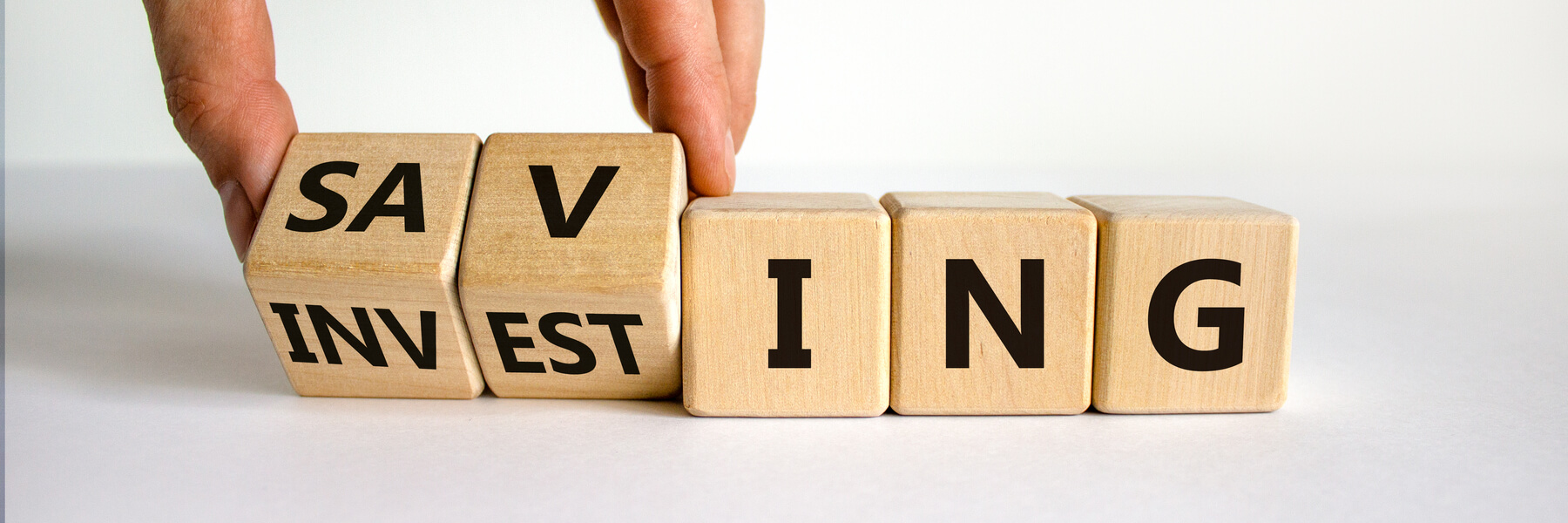 Hand placing wooden blocks down that spell out saving and investing 