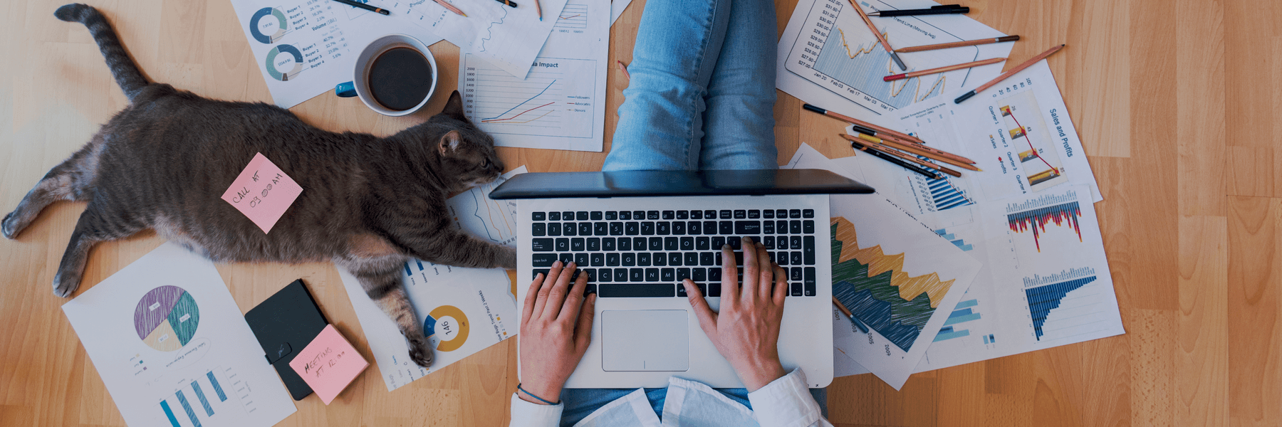 Man working on laptop with cat laying next to him and papers and pencils spread out around him