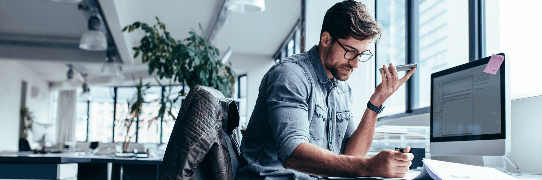 Young casual businessman holding smart phone and working in bright office