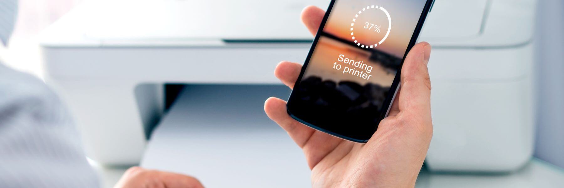 hand holding phone by printer, screen reads Sending to Printer