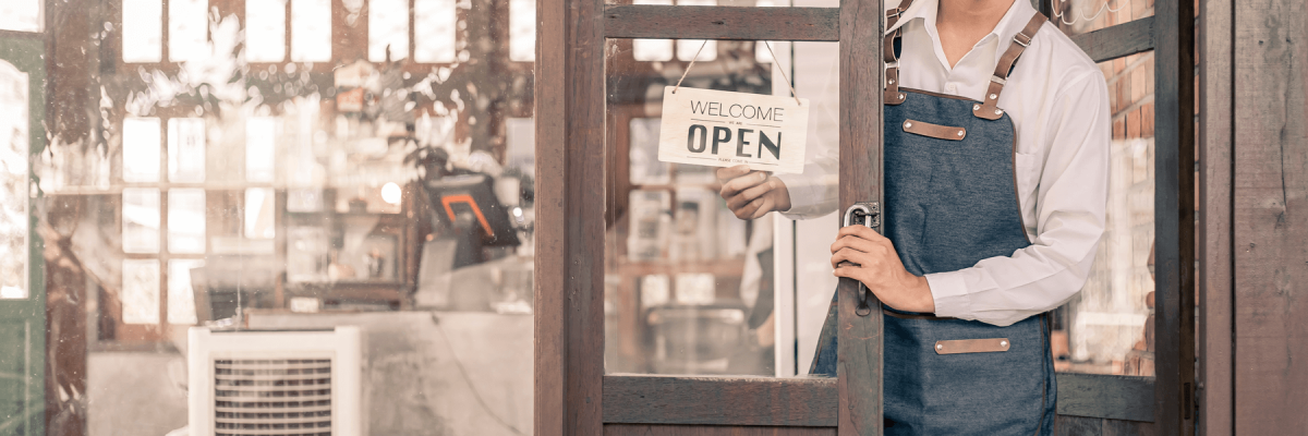 Store owner turning open sign broad through the glass door