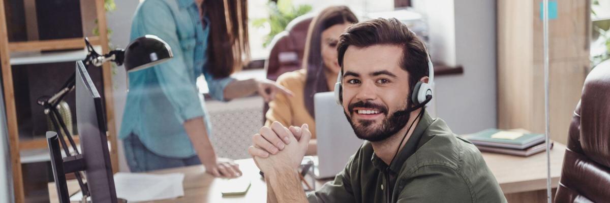 man smiling at camera; collaborating workers in background